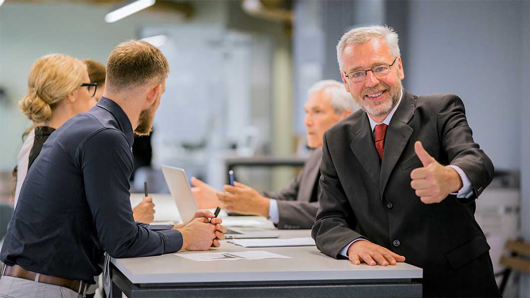 A smiling senior leader of an organization showing thumb up in the office.